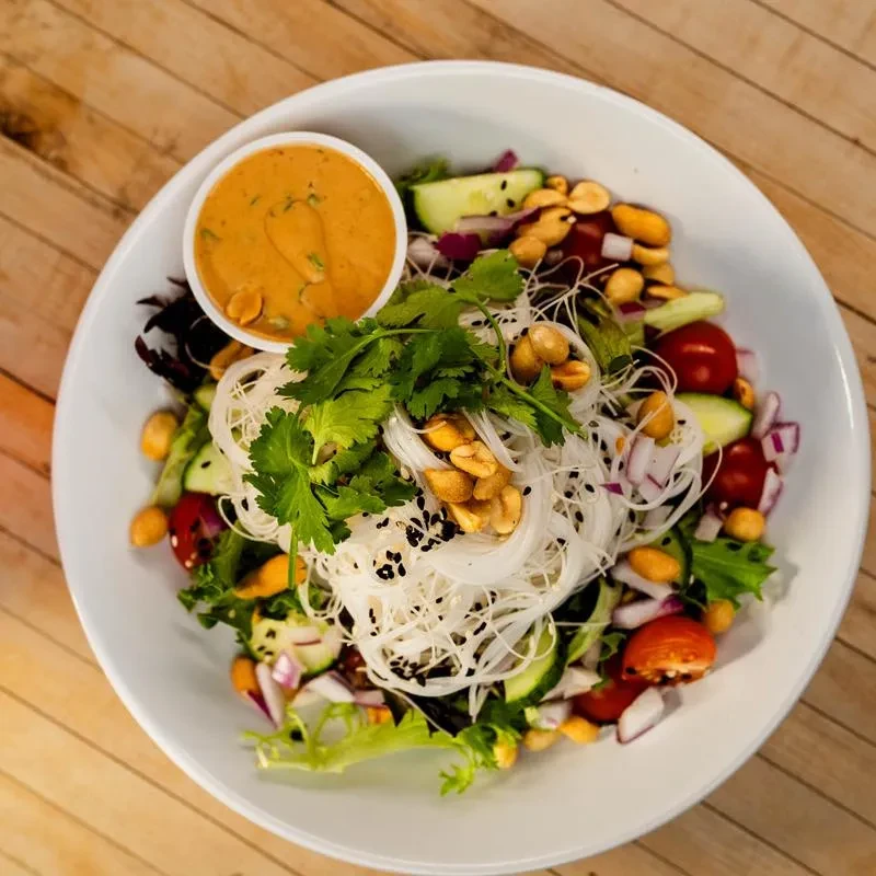 Top-down view of vibrant salad with noodles, peanuts, and dressing.