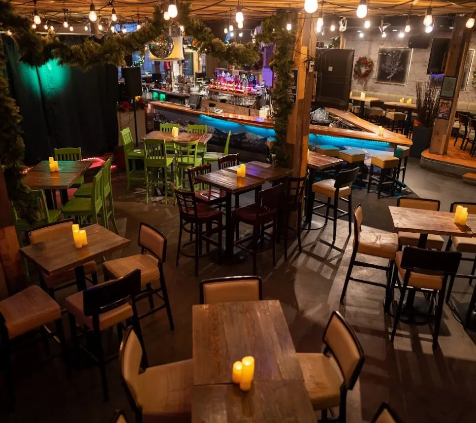 Cozy rustic restaurant interior with candlelit tables, string lights, and blue bar.