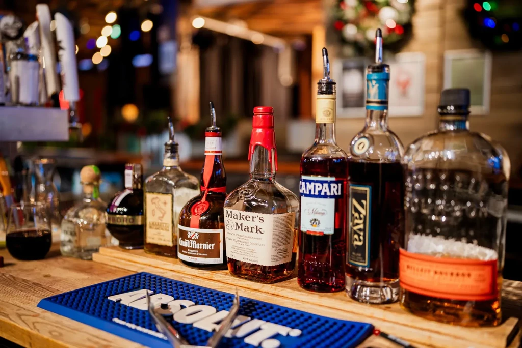Well-lit bar counter features liquor bottles, an Absolut mat, and silver tongs.
