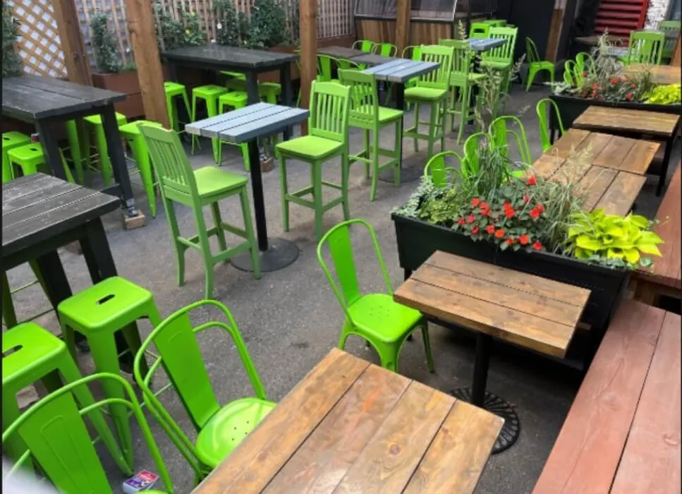 Outdoor restaurant patio with lime green chairs, dark tables, lush plants.