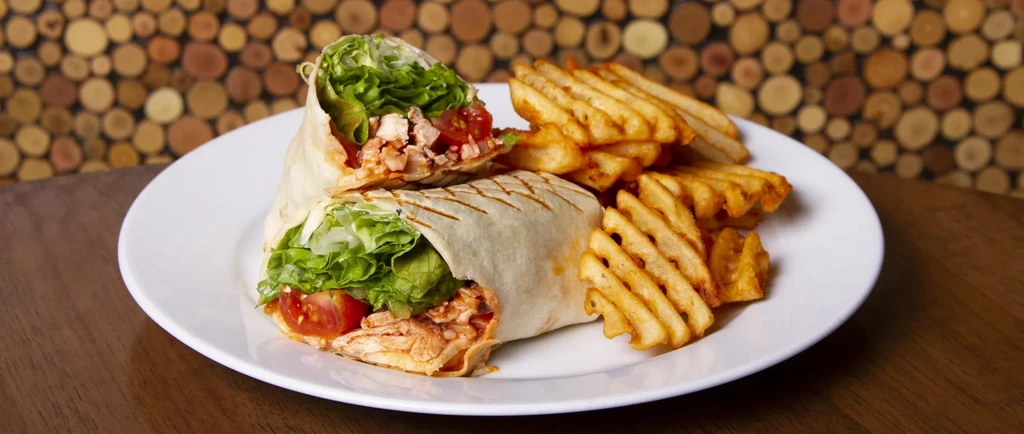 Sliced wrap showing meat and lettuce, with waffle fries.
