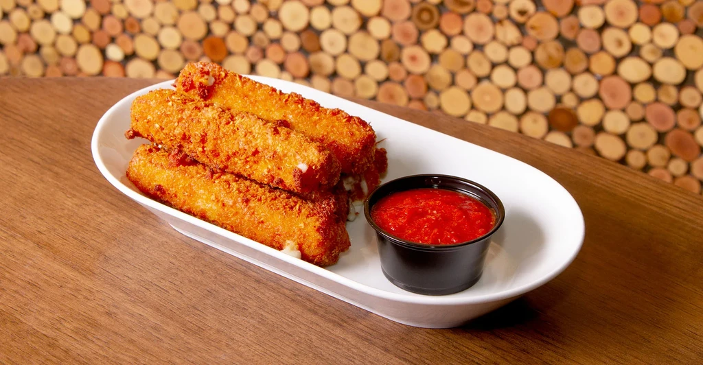 Crispy mozzarella sticks with bright red marinara, rustic setting.