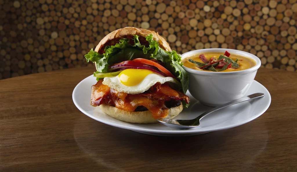 Gourmet burger with egg and bacon, next to creamy orange soup.