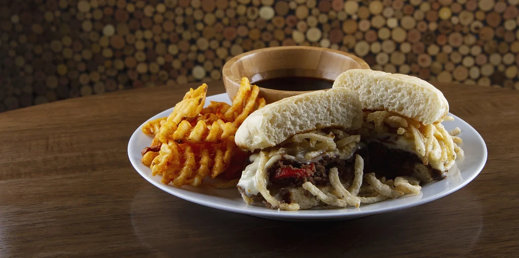 Cut sandwich, waffle fries, and dipping sauce on a dark table.