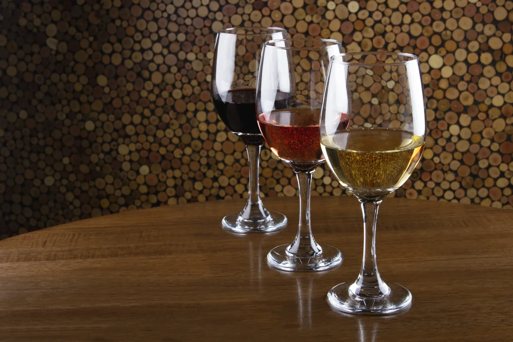 Three wine glasses, red, rosé, white wines, dark table, wood background.