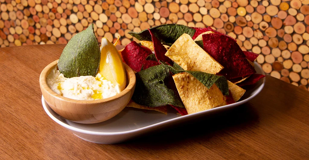 Creamy dip with citrus and colorful chips on rustic wooden table.