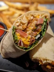 Halved chicken wrap with lettuce, cheese, tomatoes, fries, and sauce.