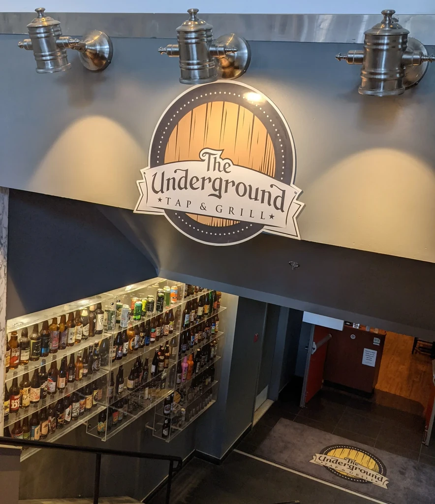 The Underground Tap & Grill entrance with logo, bottled beverages, and stairs.