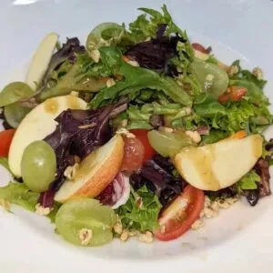 Fresh salad with lettuce, apple, grapes, tomatoes, and seeds on white plate.