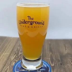 Pint glass of hazy amber beer with The Underground TAP & GRILL logo.
