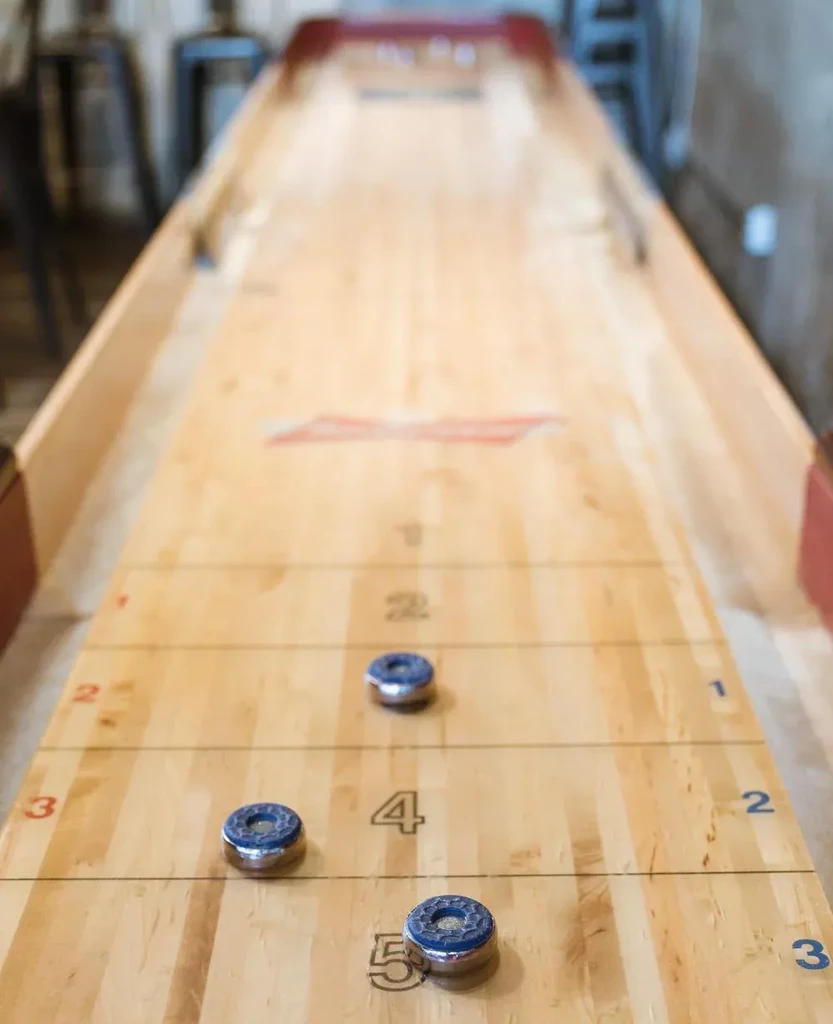 Blue pucks on a wooden shuffleboard table in a bar setting.