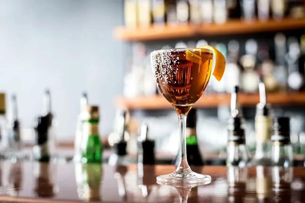 Amber cocktail in coupe glass, citrus peel, sugared rim on bar.