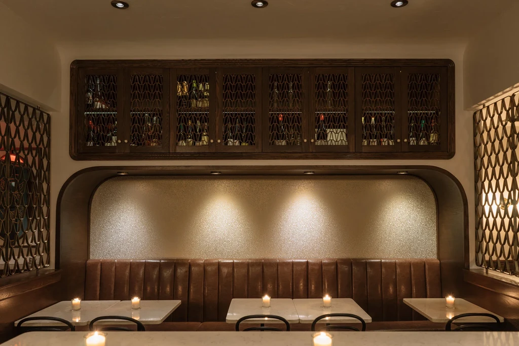 Elegant restaurant interior with cozy booths, illuminated bottles, and warm candlelight.