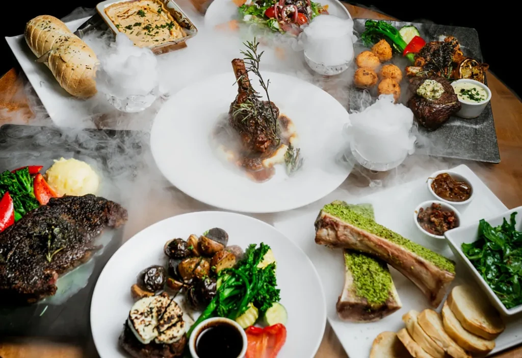 Overhead view: gourmet lamb, steaks, and bone marrow with dry ice vapor.