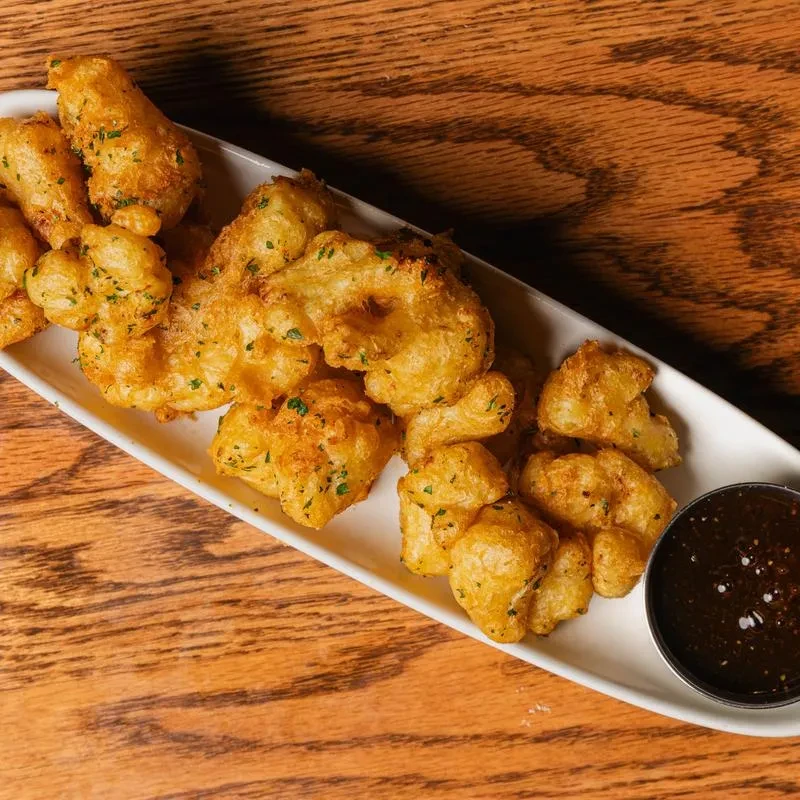 Fried golden-brown cheese curds or cauliflower with herbs and dipping sauce.