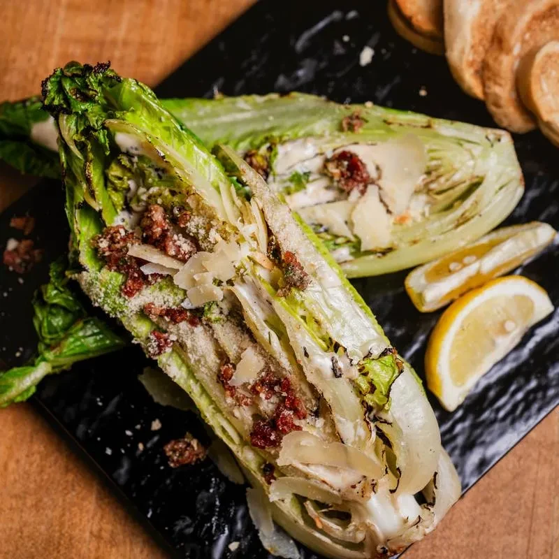 Grilled romaine salad with dressing, Parmesan, bacon, and lemon wedges.