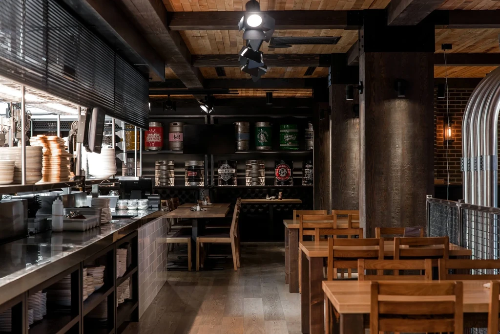 Empty rustic-industrial restaurant with beer keg wall and kitchen counter.