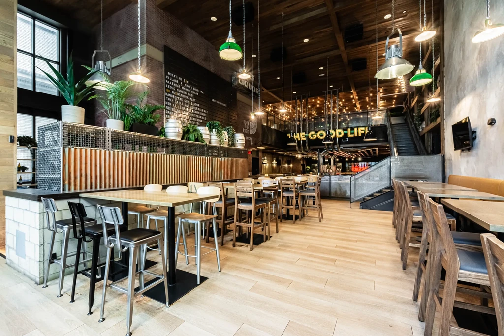 Spacious, modern industrial restaurant with bar, staircase, and neon sign.