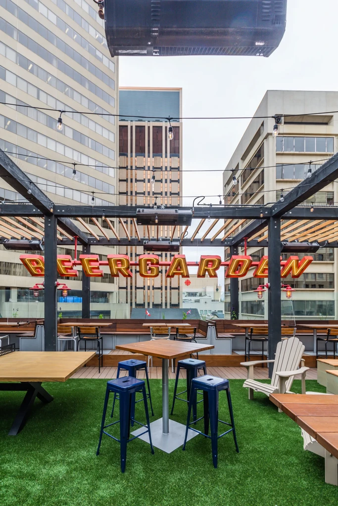 Rooftop beergarden with turf, seating, string lights, and city background.