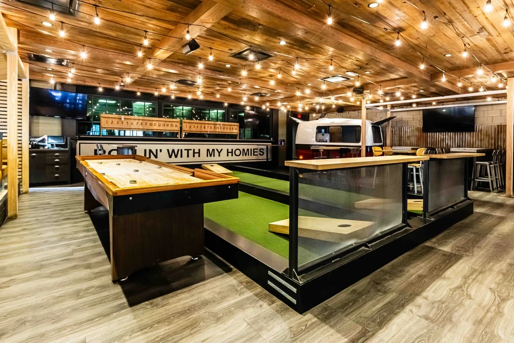 Modern gastropub interior featuring shuffleboard, cornhole, and a camper bar.