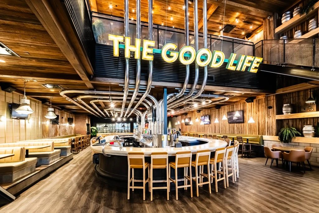 Modern industrial bar with "THE GOOD LIFE" neon sign and beer taps.