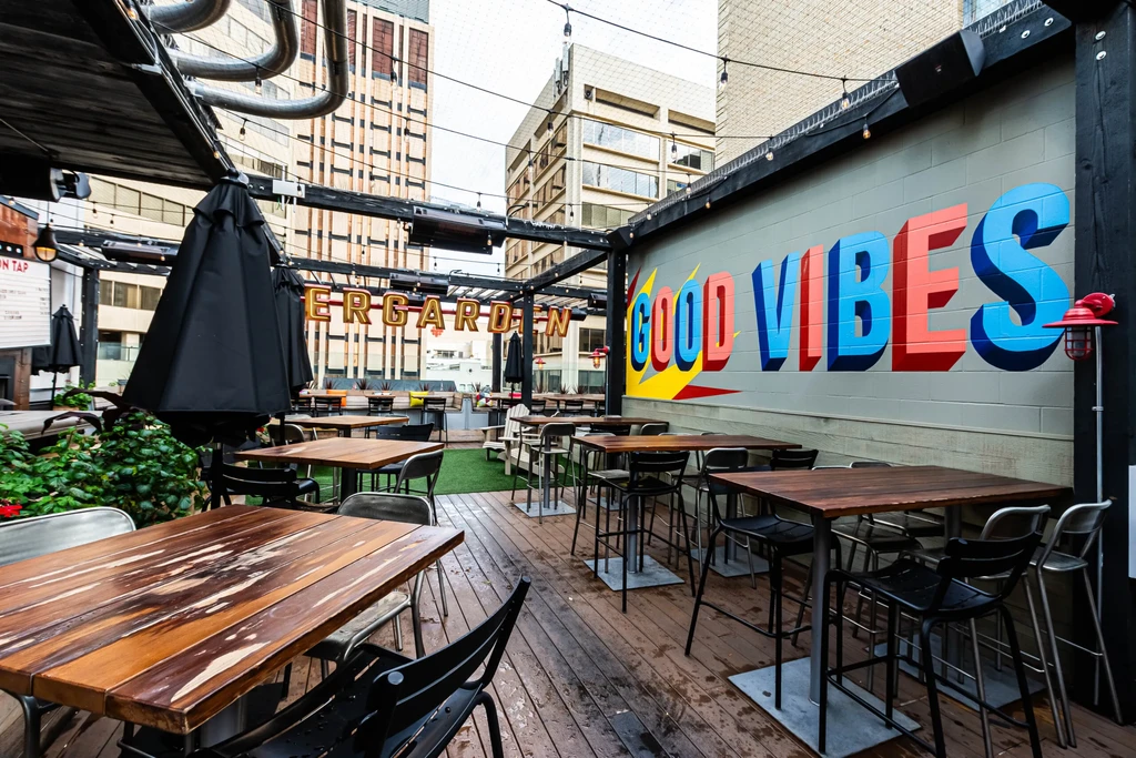 Empty urban rooftop patio with tables, string lights, and "GOOD VIBES" mural.