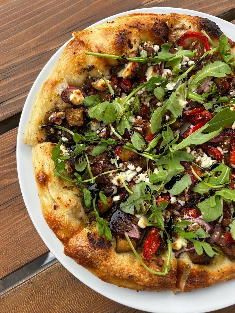 Flatbread with roasted vegetables, feta, arugula, and balsamic glaze on wood.