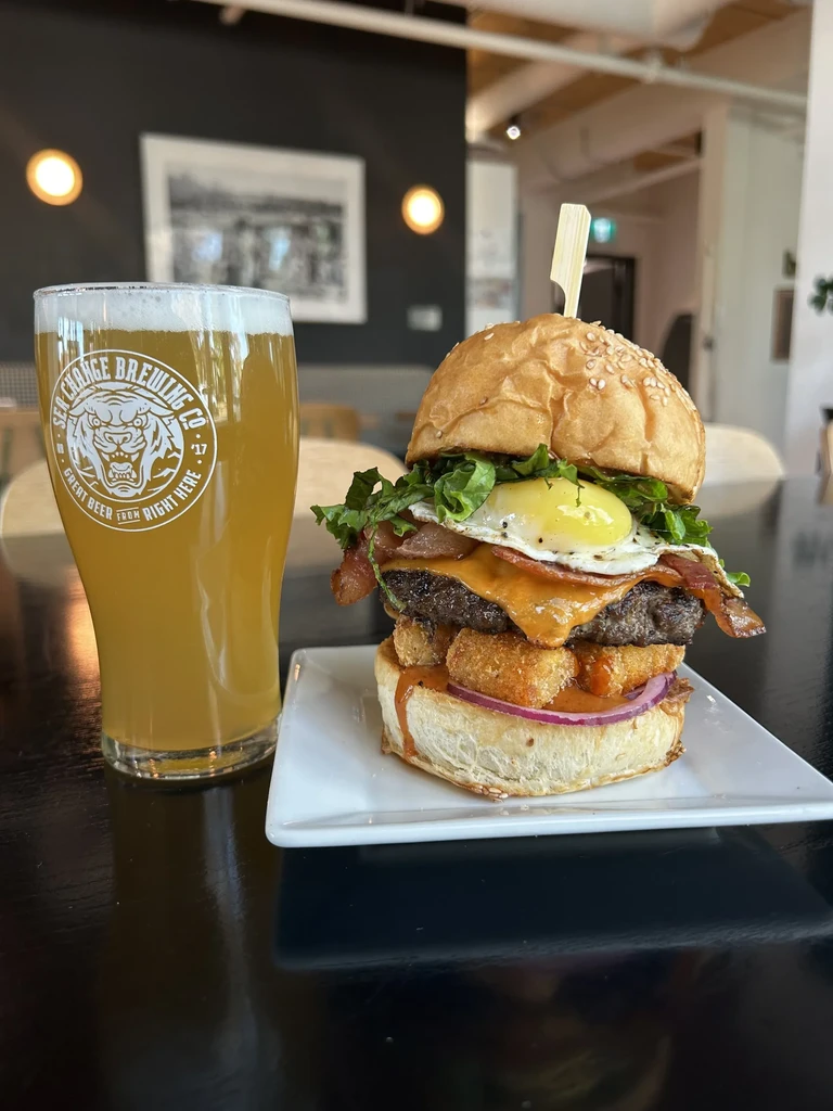 Gourmet burger with fried egg and bacon, next to a pint of beer.