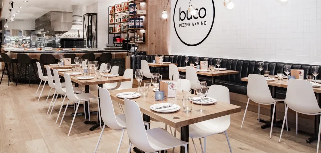 Bright, modern pizzeria interior with dining tables, bar, and kitchen.