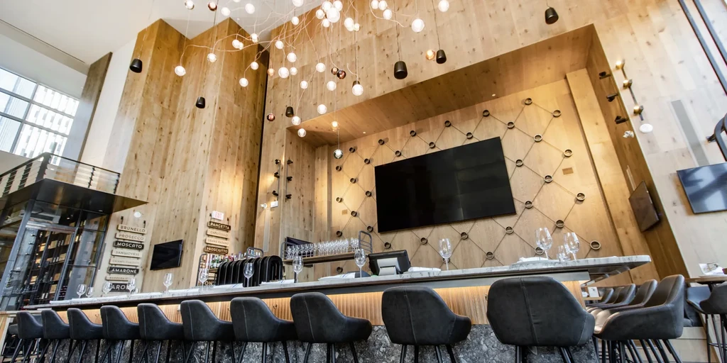 Modern upscale bar interior with marble counter, wood walls, and chandelier.