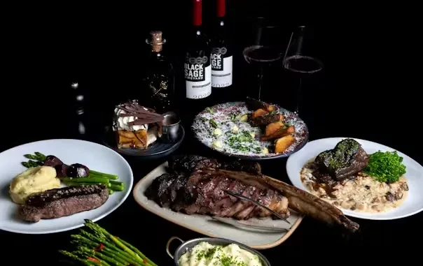 Gourmet food spread with tomahawk steak, short ribs, and Black Sage wine.