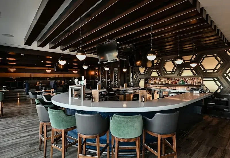 Modern restaurant bar featuring a curved counter and illuminated liquor wall.