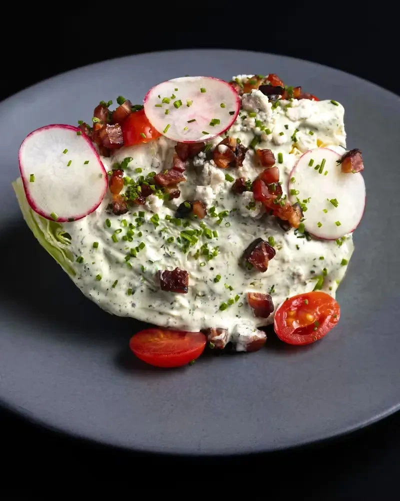 Wedge salad with creamy dressing, bacon, blue cheese, chives, radish, tomatoes.
