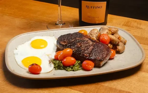 Grilled steak, sunny-side eggs, roasted potatoes, tomatoes, and pesto.