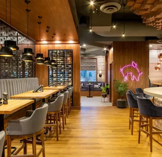 Modern restaurant interior with dining area, bar, and pig neon sign.