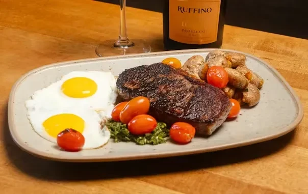 Plate of seared steak, fried eggs, potatoes, tomatoes, and Ruffino Prosecco.