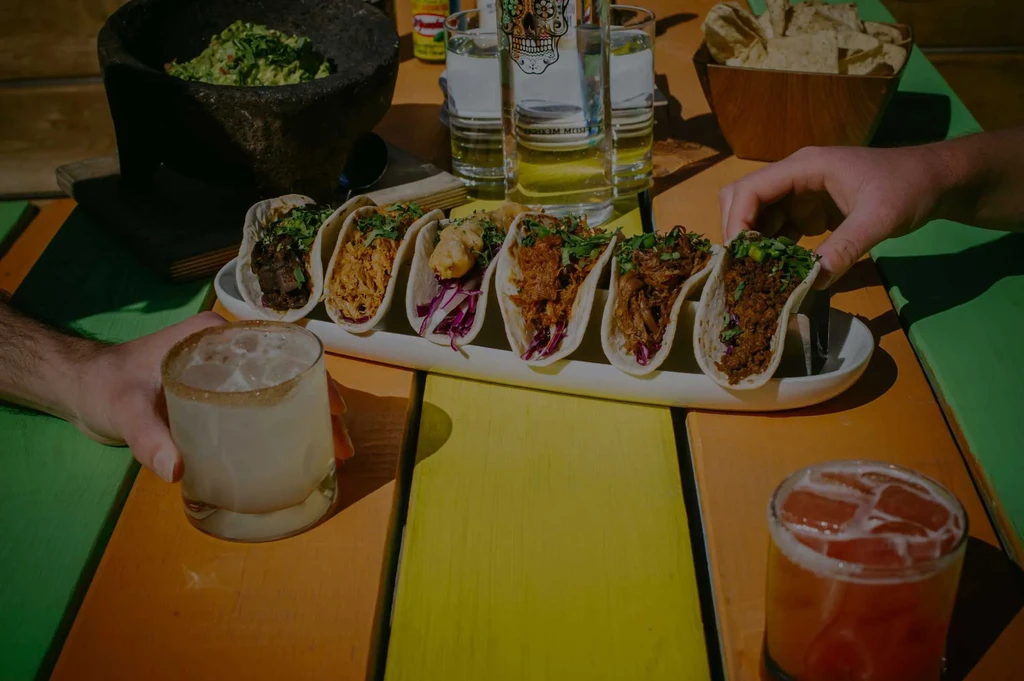 Tacos, guacamole, and drinks on a vibrant striped wooden table.