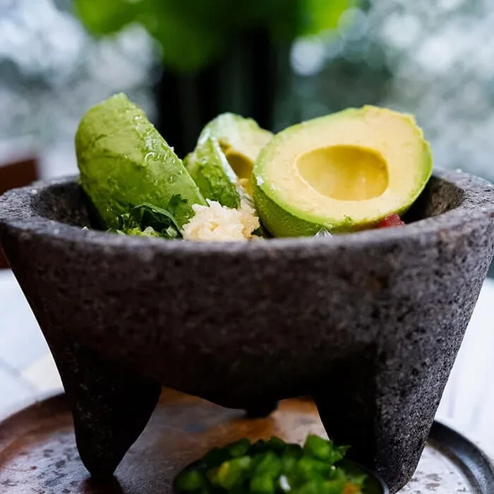 Fresh guacamole ingredients in a molcajete: avocados, cilantro, onions, and peppers.