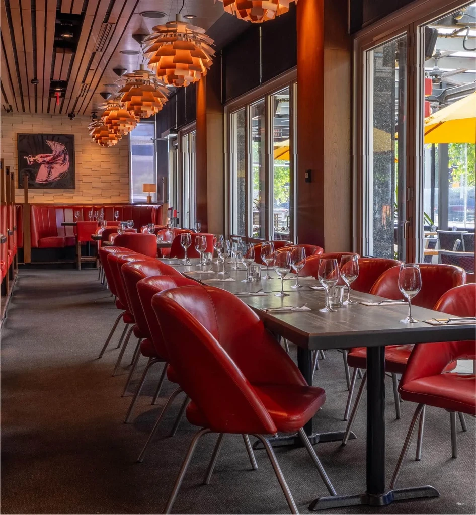 Empty modern restaurant with red chairs, geometric lights, and patio.
