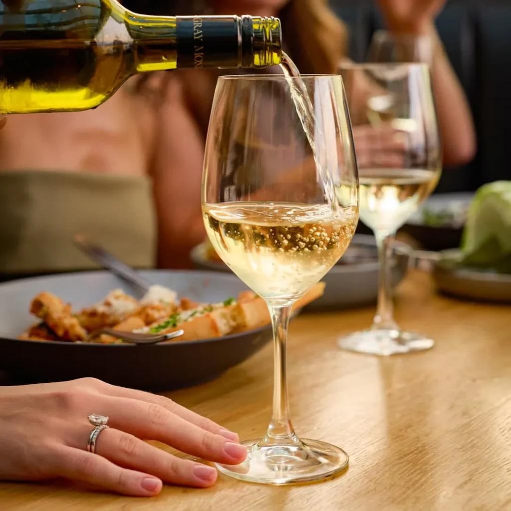 Gray Mont white wine pouring into goblet, hand with rings.