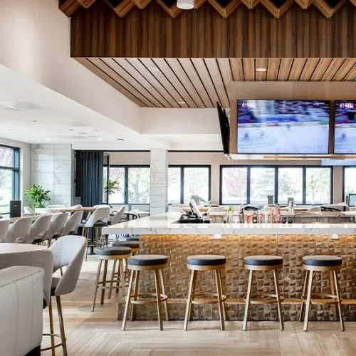 Modern restaurant bar interior featuring gold-paneled counter, TVs, and dining.