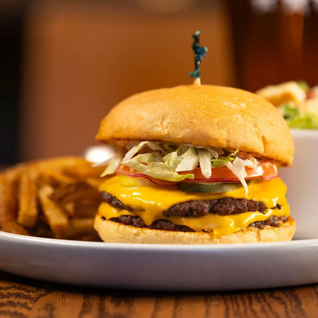 Close-up of a double cheeseburger with melted cheese, lettuce, pickles, and fries.
