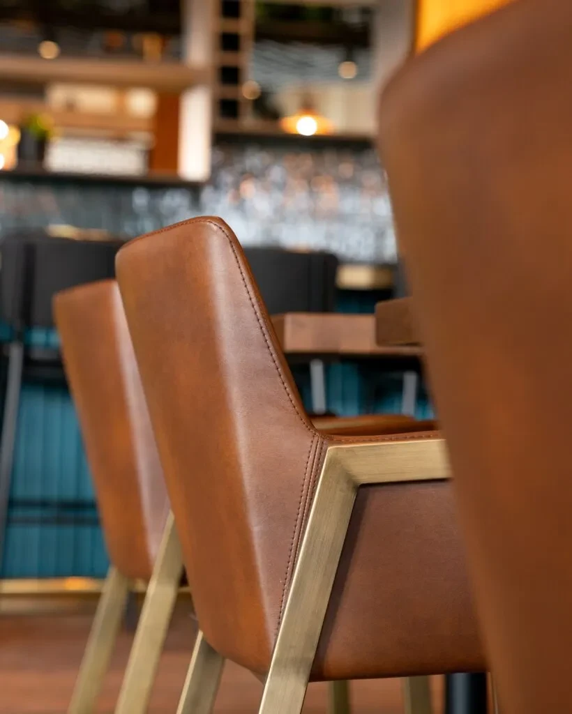 Two modern brown leather bar stools with brass frames and stitching.