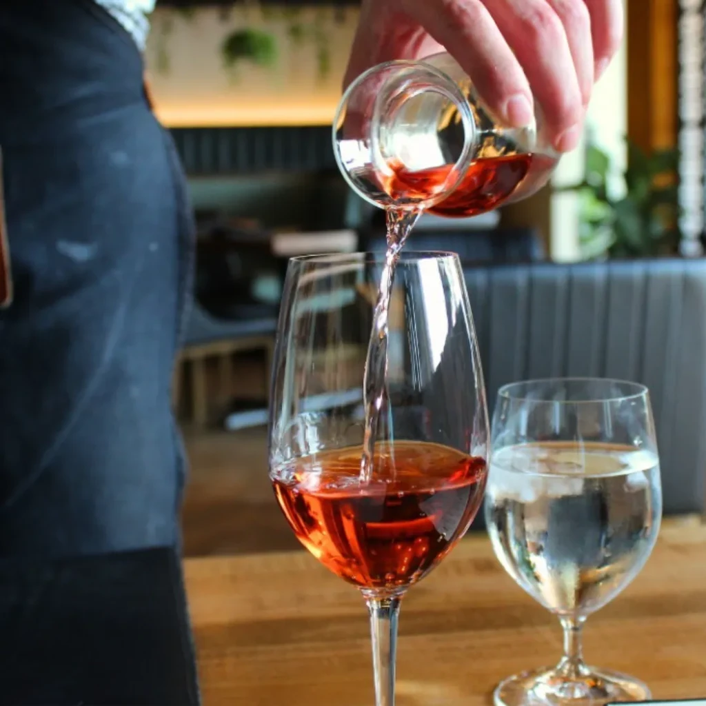 Hand pouring rosé wine from carafe into wine glass.