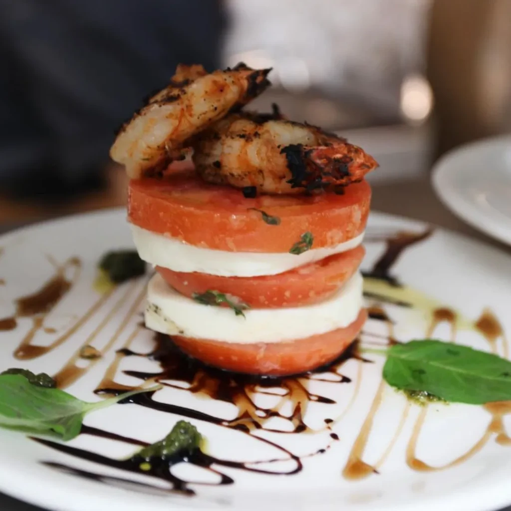 Plated caprese salad stack with grilled shrimp, balsamic, and pesto.