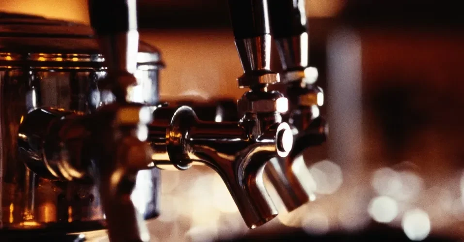 Close-up of several metallic beverage taps in a dimly lit bar.