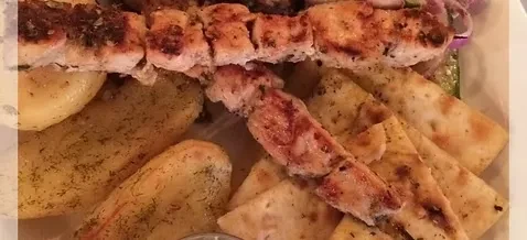 Grilled chicken skewers, roasted potatoes, and pita bread on a white plate.