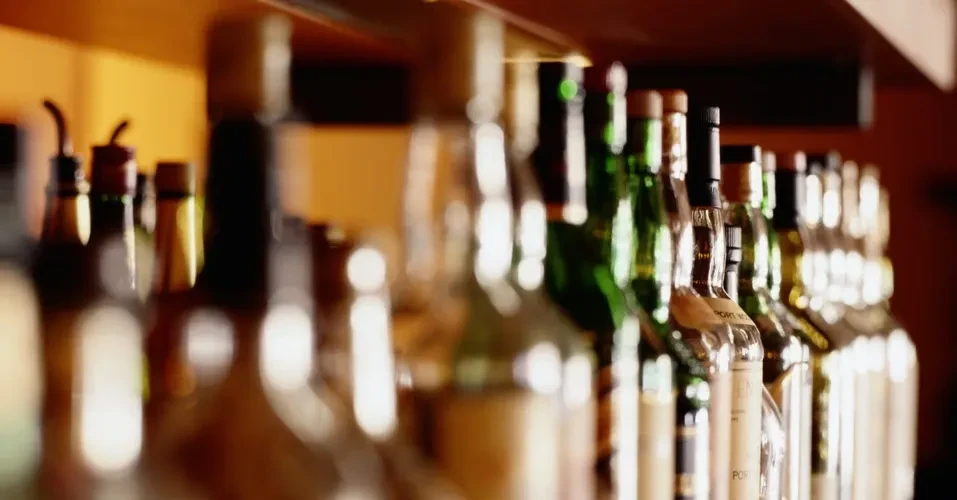 Warmly lit liquor bottles on a bar, some with pour spouts.