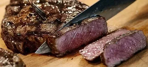Seared medium-rare steak sliced by a knife on a wooden board.