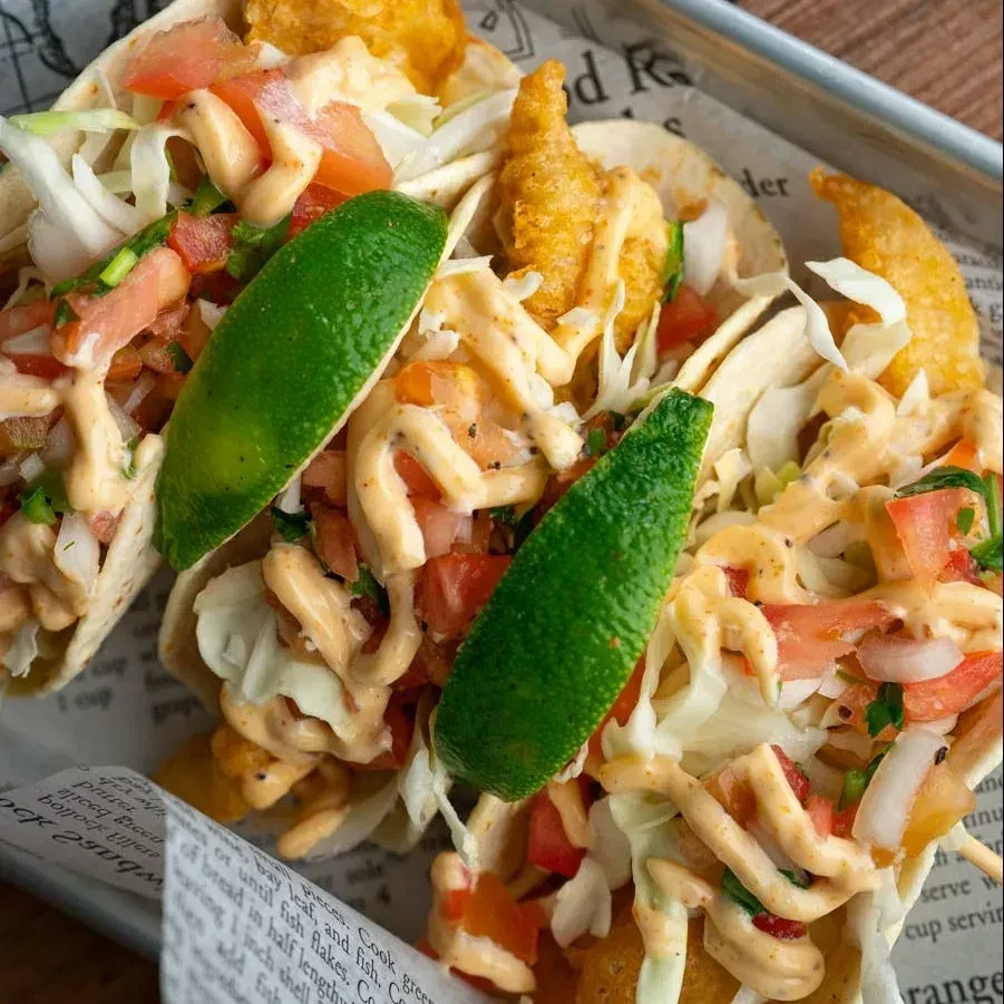 Three fried seafood tacos with pico de gallo, sauce, and lime.